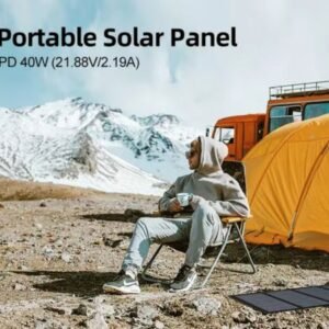 A person sits outdoors in a chair, nestled in a rocky mountain terrain with snowy peaks in the background. They are near a yellow tent and an orange vehicle, holding a mug. A power bank is connected to a portable solar panel laying on the ground nearby. Text above reads, "Portable Solar Panel PD 40W (21.88V/2.19A).