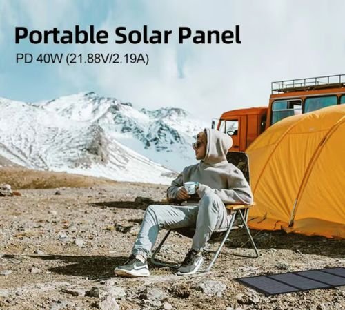 A person sits outdoors in a chair, nestled in a rocky mountain terrain with snowy peaks in the background. They are near a yellow tent and an orange vehicle, holding a mug. A power bank is connected to a portable solar panel laying on the ground nearby. Text above reads, "Portable Solar Panel PD 40W (21.88V/2.19A).