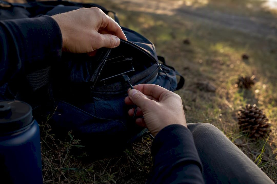 Hiker connecting charger cable in backpack outdoors
