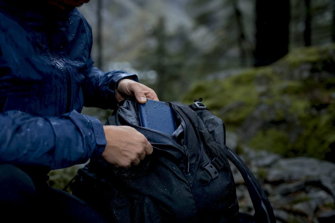 Hand securing power bank in rain-soaked backpack pocket