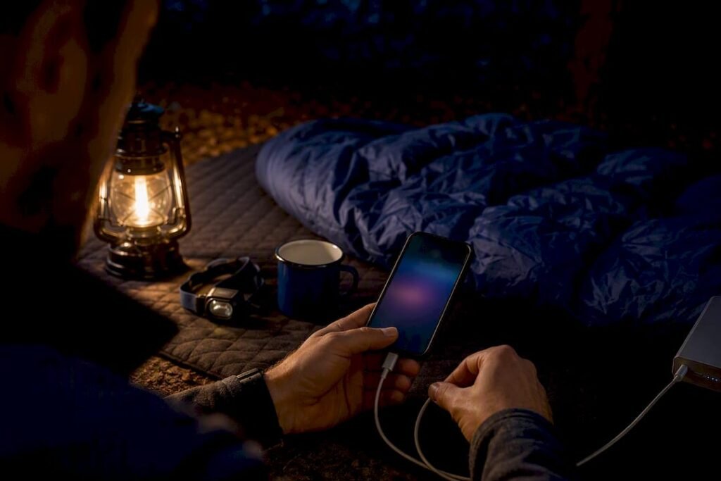 Camper charging phone beside tent at night